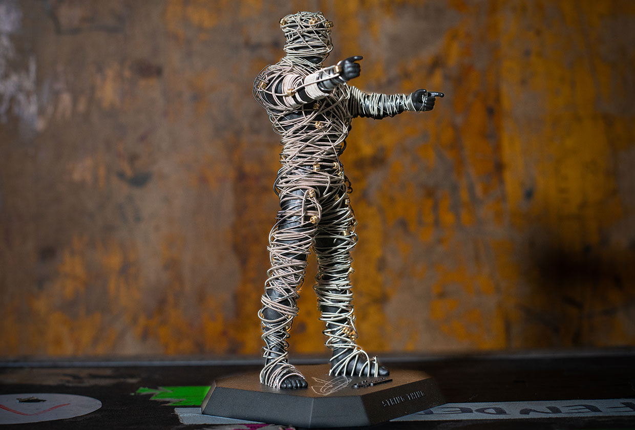 A closer view of the String Thing figure showing the wrapped guitar strings and workbench surroundings