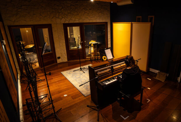 A student plays a keyboard while recording in SAE Institute Amsterdam's live room, with isolation booths visible in the background